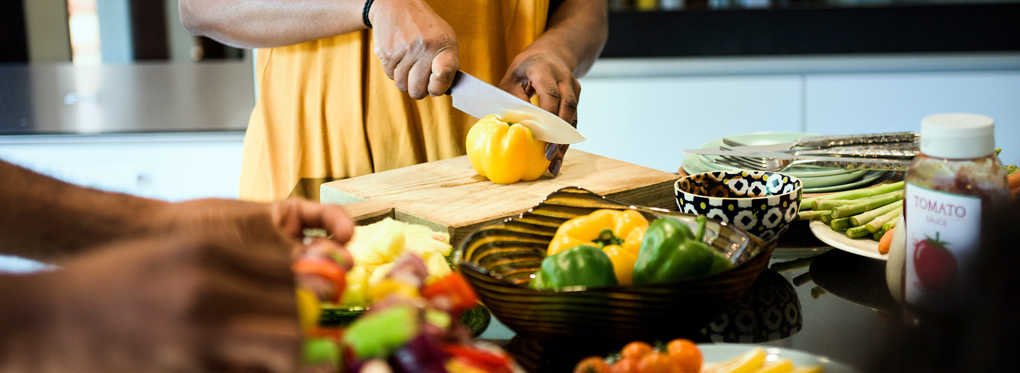 A woman cutting a pepper on a cutting board with other vegetables in the foreground