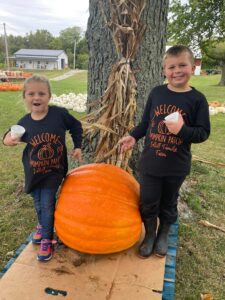 two kids with a large pumpkin between them standing by a tree