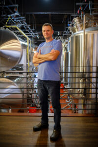 Chef James portrait in front of commercial beer brewing equipment.