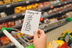 Woman with notebook in grocery store, closeup. Shopping list on paper. Check purchases in grocery cart.