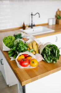 Fresh vegetables and fruits in eco cotton reusable bags on wooden table in the kitchen. zero waste shopping concept. Sustainable living